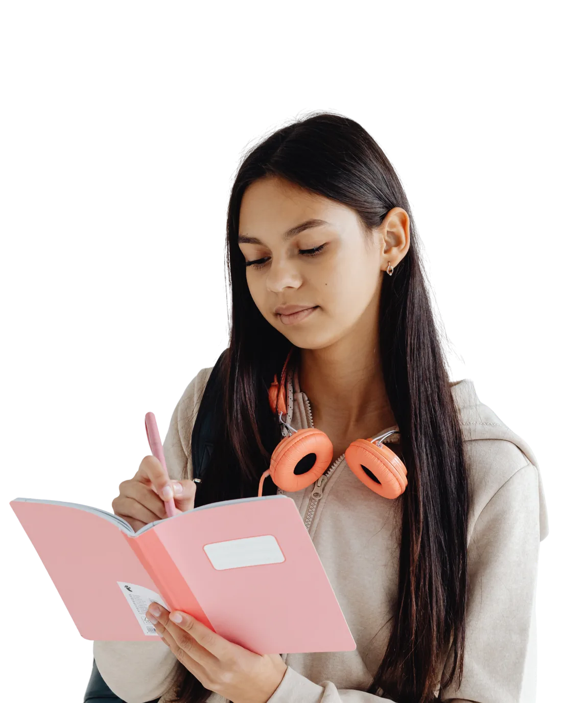 A student writing in a notebook, headphones around her neck.